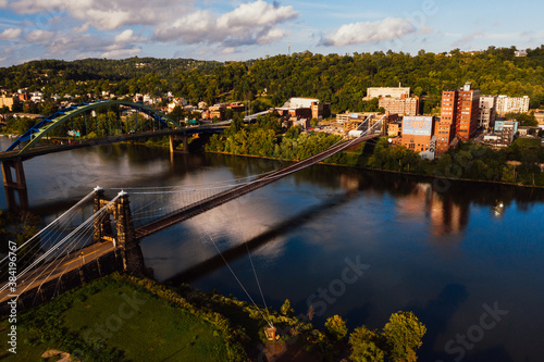 This is an aerial view of the historic Wheeling Suspension Bridge that carries the National Road over the still blue waters of the Ohio River in Wheeling, West Virginia.