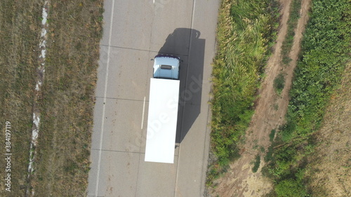 Aerial view of truck with white cargo trailer driving on empty road and transporting goods. Flying over one delivery lorry moving through country highway. Logistic concept. Top view