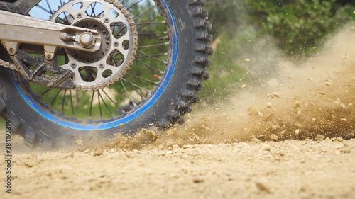 Close up wheel of powerful off-road motorcycle spinning and kicking up dry ground. Professional motocross rider starting race or training. Active lifestyle concept. Side view Slow motion