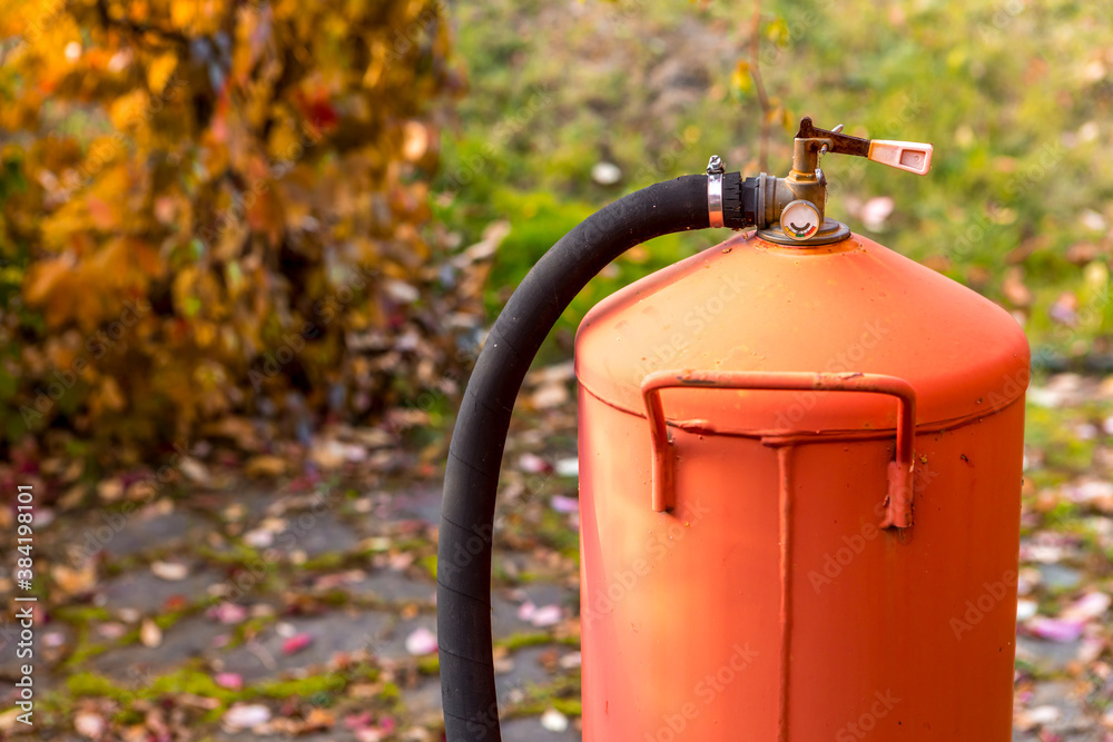 A cylinder of liquefied gas stands against a background of yellow leaves A cylinder of liquefied gas stands against a background of yellow leaves