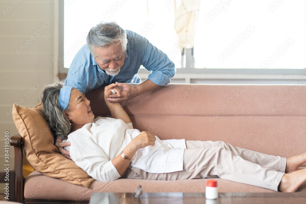 Asian Elderly couple at home. Old woman in pain lying on sofa with senior husband at home
