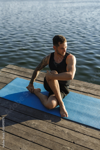 Image of healthy man stretching his body at sports ground outdoors