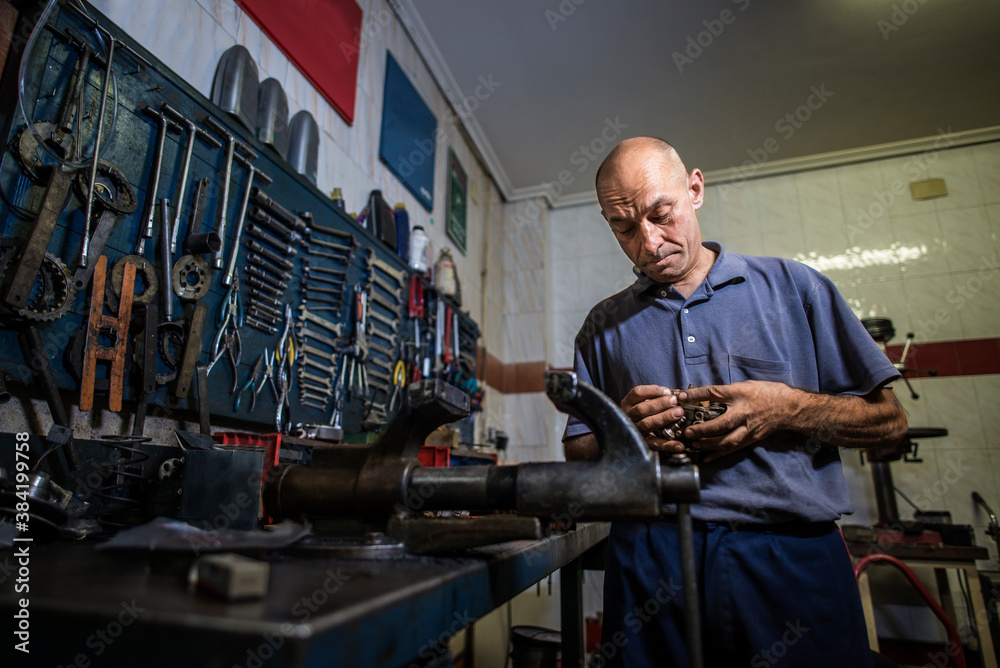 © Antonio Recena - Old mechanic working in his workshop of motorcycles and mopeds. Ambient light,