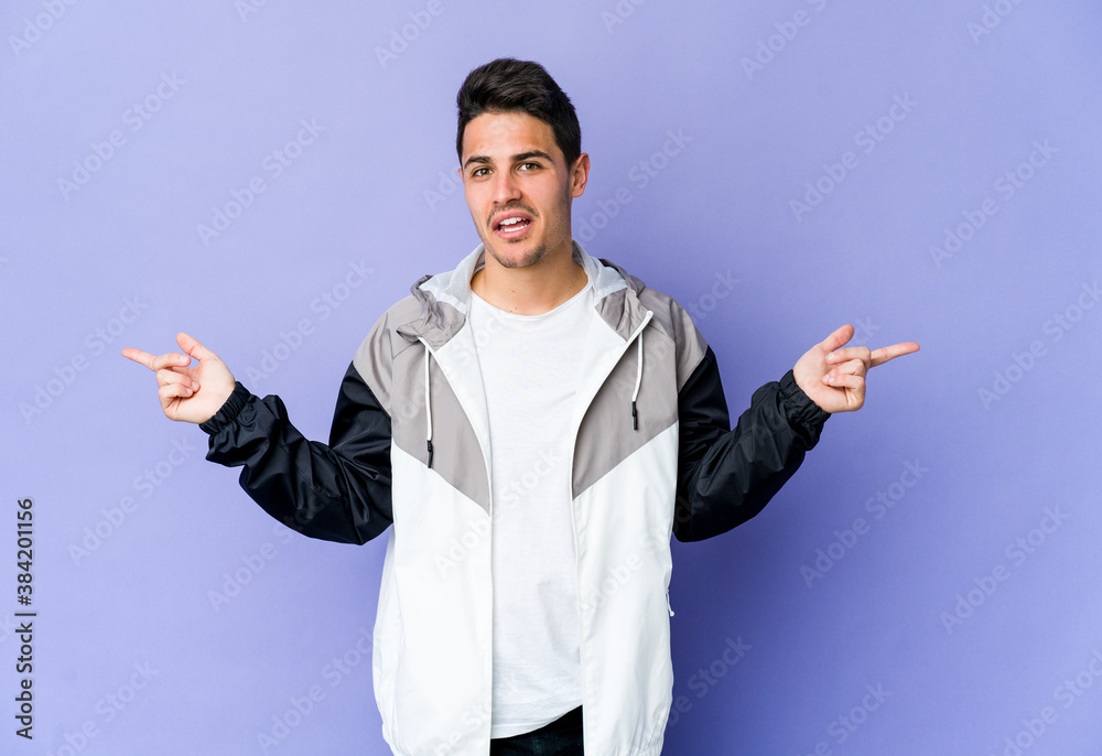 Young caucasian man isolated on purple background pointing to different copy spaces, choosing one of them, showing with finger. Young caucasian man isolated on purple background pointing to different copy spaces, choosing one of them, showing with finger.