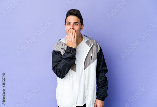 Young caucasian man isolated on purple background shocked, covering mouth with hands, anxious to discover something new.