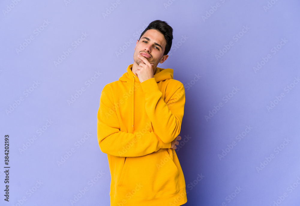Young caucasian man isolated on purple background thinking and looking up, being reflective, contemplating, having a fantasy.