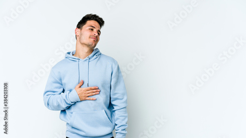 Young caucasian man isolated on white background touches tummy, smiles gently, eating and satisfaction concept.