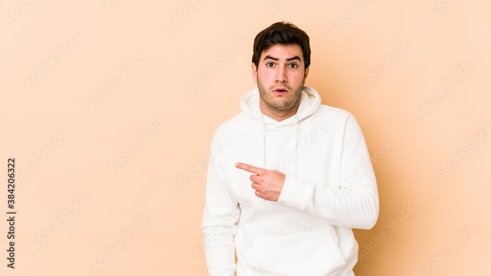 Young man isolated on beige background pointing to the side Young man isolated on beige background pointing to the side