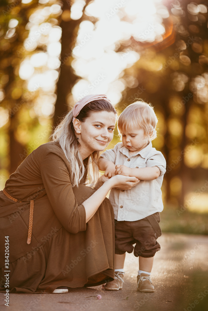 Obraz premium A young mother helps her son start walking. A mother teaches her son, educates him, and takes care of him.