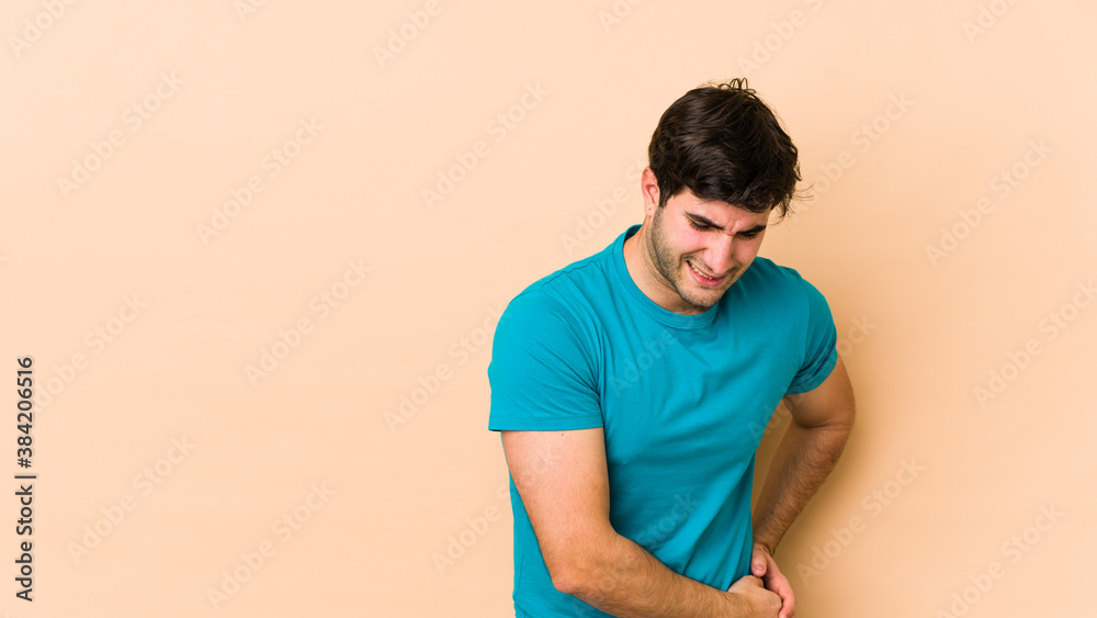 Young man isolated on beige background having a liver pain, stomach ache. Young man isolated on beige background having a liver pain, stomach ache.