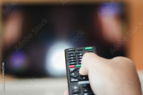 Close-up of hand with the remote control television and presses the button. Television remote control changes channels thumb on the blue TV screen.