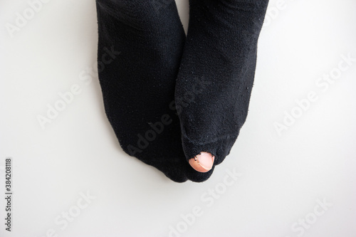 Caucasian male toe sticking out of worn out short nylon black plain socks with hole top view