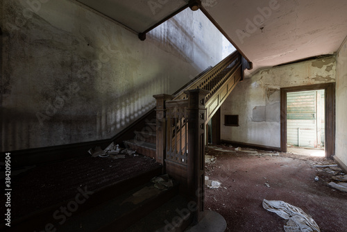 This is an interior view of the first-floor foyer with a stunning wood-paneled staircase at the long-abandoned and historic Dunnington Mansion in Farmville  Virginia.
