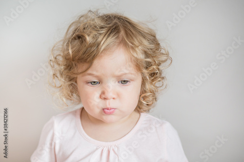 Emotional curly baby girl looking down on light gray background 