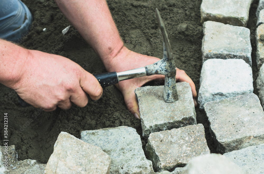 setzen eins Porphyr Pflastersteins mit dem Hammer auf einer Baustelle. Der Stein wird in Beton gesetzt. Der Hammer liegt auf dem Pflasterstein.