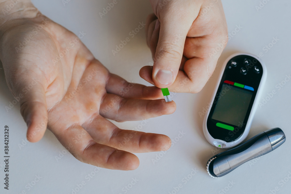 diabetes, healthcare - close up of a man with a glucometer and a test strip checking blood sugar at home diabetes, healthcare - close up of a man with a glucometer and a test strip checking blood sugar at home