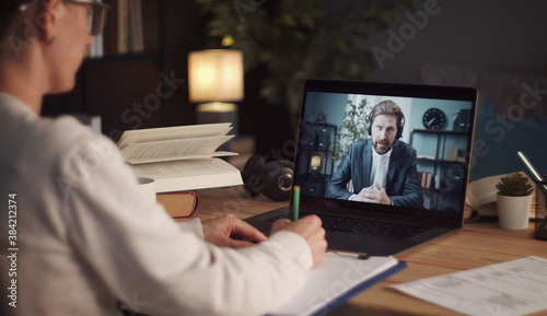 Overshoulder view of woman making notes talking to male business partner using video call photo