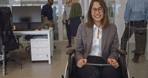 Disabled business woman in wheelchair holding table smiling in office photo