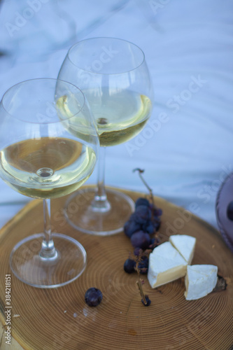 wooden stand with two glasses of champagne, grapes and camembert cheese on a white blanket in the field. picnic.