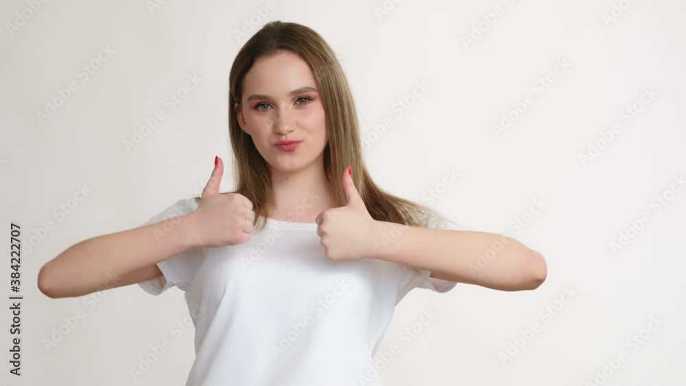 Like sign. Perfect choice. Amused teen girl in white t-shirt with braces smiling supporting showing thumbs up gesture isolated on light copy space background. Encouragement accept. Like sign. Perfect choice. Amused teen girl in white t-shirt with braces smiling supporting showing thumbs up gesture isolated on light copy space background. Encouragement accept.