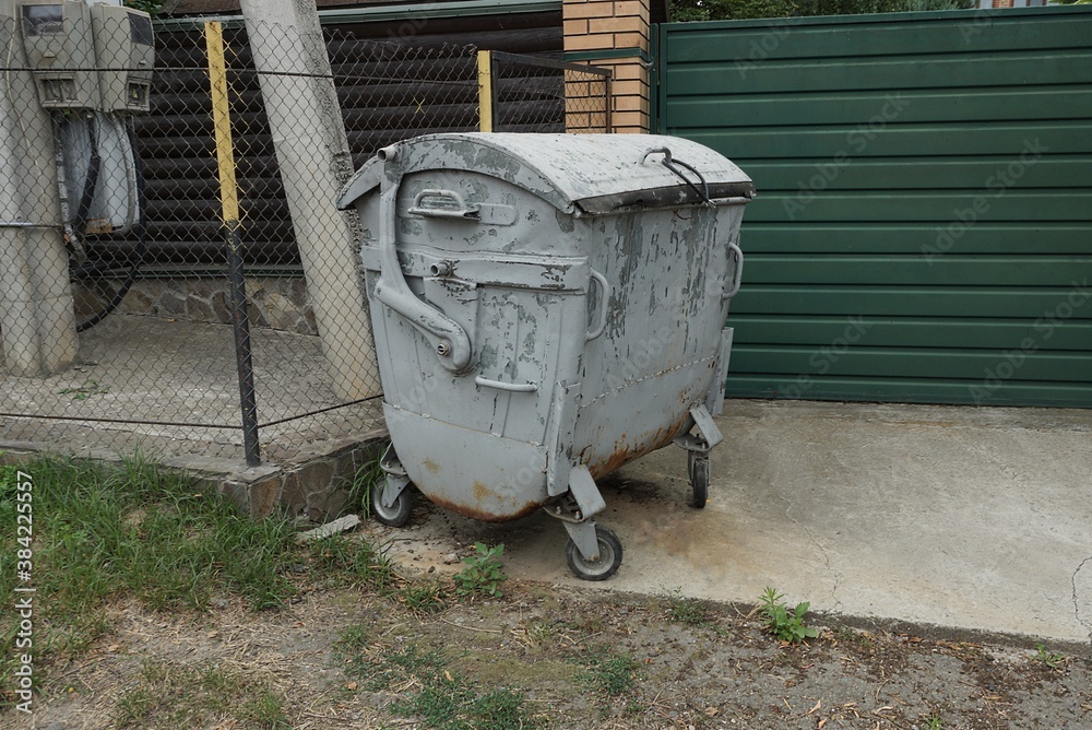 one gray closed metal trash can stands on the street against the wall one gray closed metal trash can stands on the street against the wall