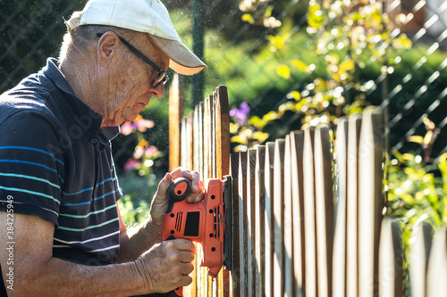 Bild auf Leinwand Senior man sanding wooden fence with electric sander in garden