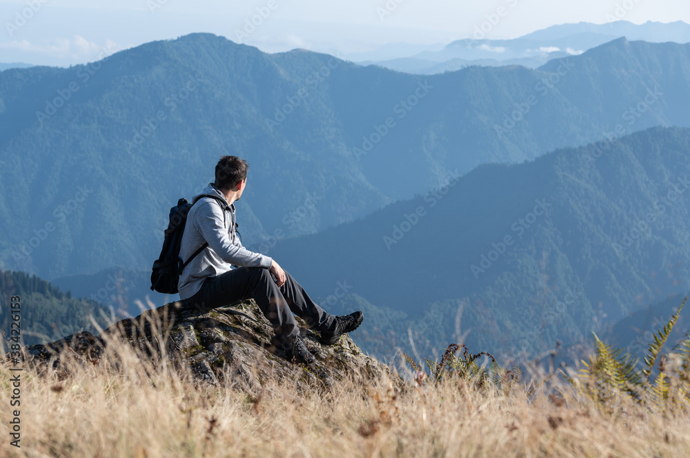 Young man sitting on the rock and enjoying blue mountains range view Young man sitting on the rock and enjoying blue mountains range view