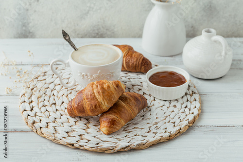 Delicious breakfast with fresh croissants and cup of coffee served with jam on a white wooden background. Delicious Baking