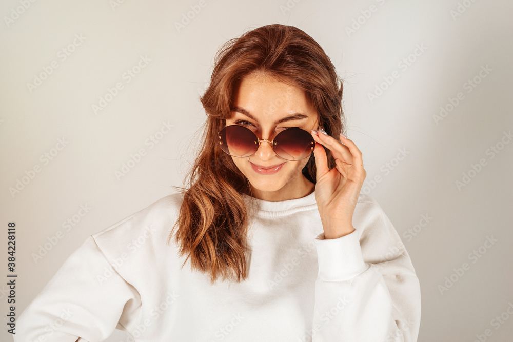 Woman is winking against a bright white background wearing sunglasses