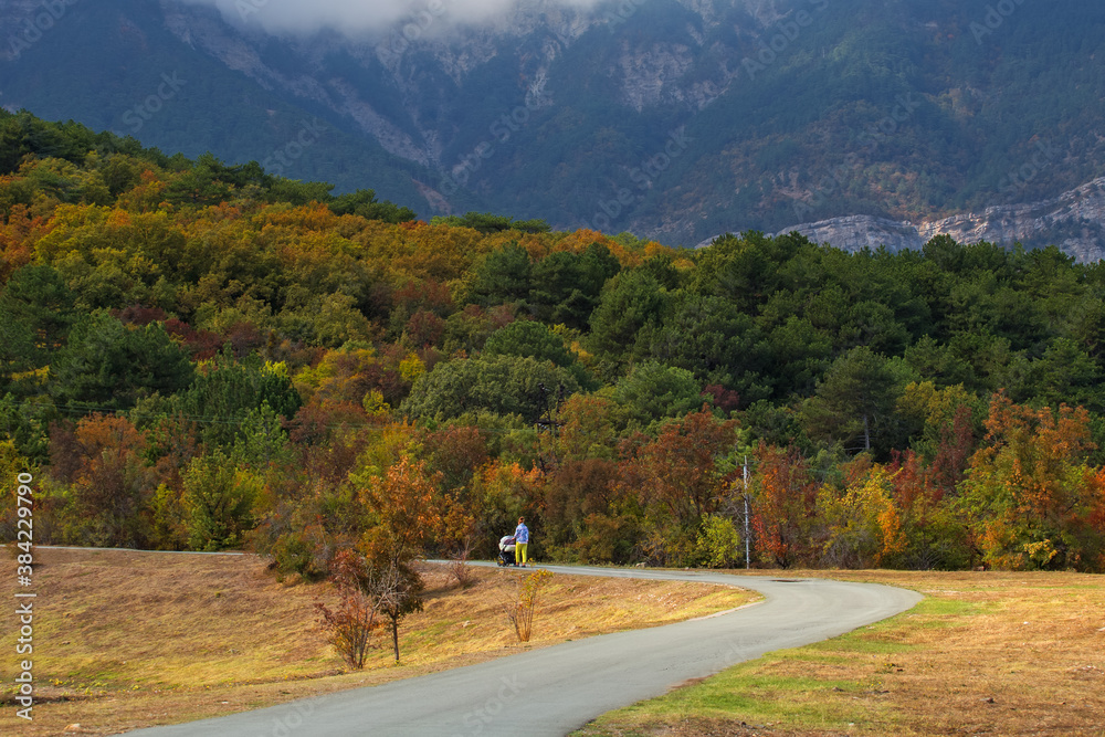 Very beautiful colorful autumn landscape. Paved road in the mountains in autumn. A girl with a stroller in the Park is walking along the autumn road.