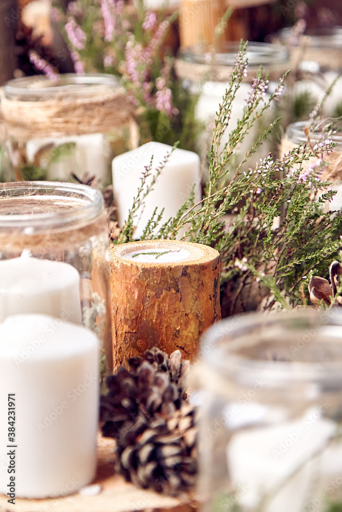 still life consisting of white candles, wood, pine cones and glass jars, with a blurred background and green grass