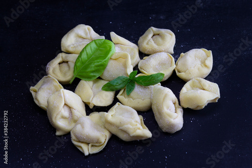 Fresh Ravioli with basil on floury dark background. Italian homemade healthy food concept.Process of making italian pesto ravioli.