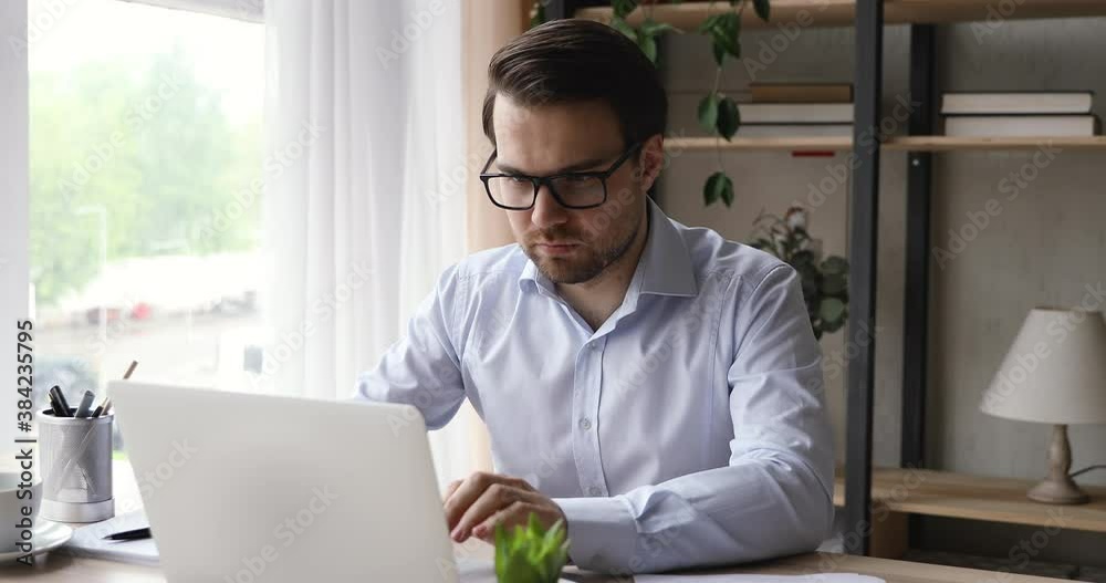 Happy young man in eyeglasses getting email with good news on computer, celebrating professional achievement or good luck success, reading online lottery win notification, positive emotion reaction.