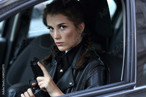 Tablou pe pânză Girl driving a car with a gun in her hands