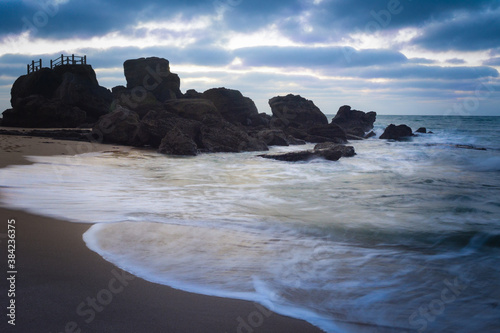 Beach with waves next to rocks in cloudy day
