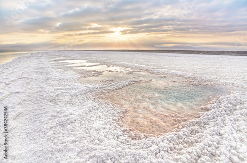 Crystalline white salt beach lit by morning sun, small pools with seawater at Dead Sea - world most hypersaline lake