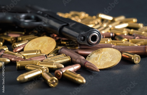 Bronze and brass gun bullets scattered on dark table, black pistol barrel, golden bitcoin coins near - illegal use of cryptocurrency to purchase weapon concept
