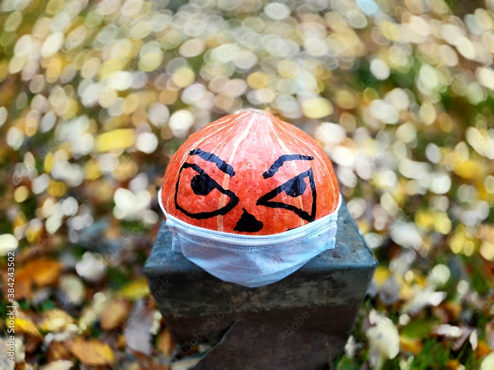 Halloween pumpkin in disposable mask on blurred background of autumn and colored leaves