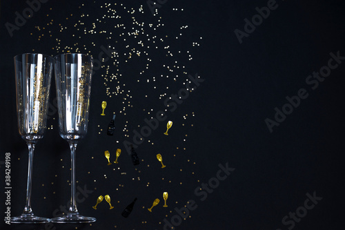 Two champagne glasses, golden confetti on a festive black background. Festive Christmas, New Year concept. Copy space.