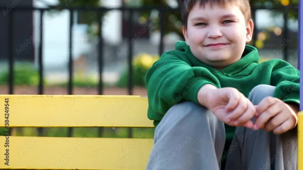 Portrait of happy kid boy looking at camera smiling having fun on the swing at the school playground. cute young child sitting on a bench laughing and dreaming. Active toddler playing in the park. Portrait of happy kid boy looking at camera smiling having fun on the swing at the school playground. cute young child sitting on a bench laughing and dreaming. Active toddler playing in the park.