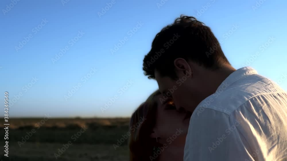 Slowmo of kissing caucasian couple in summer field. Man and woman are looking at each other with affection and tenderness. Romantic date in outdoors. Cute falling in love pair on blue sky background. Slowmo of kissing caucasian couple in summer field. Man and woman are looking at each other with affection and tenderness. Romantic date in outdoors. Cute falling in love pair on blue sky background.