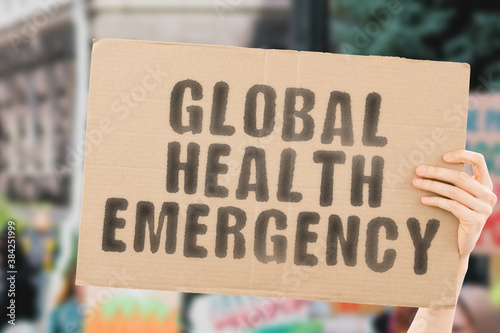 The phrase " Global health emergency " on a banner in men's hand with blurred background. Health. Dangerous. Hospital. Healthcare. Hazardous. Crisis. Collapse