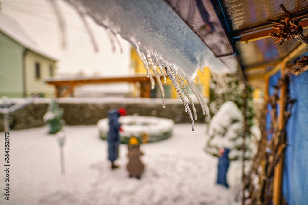 Icicles hanging from house roof in a garden with a blurry family in the background - typical winter scenery. Icicles hanging from house roof in a garden with a blurry family in the background - typical winter scenery.