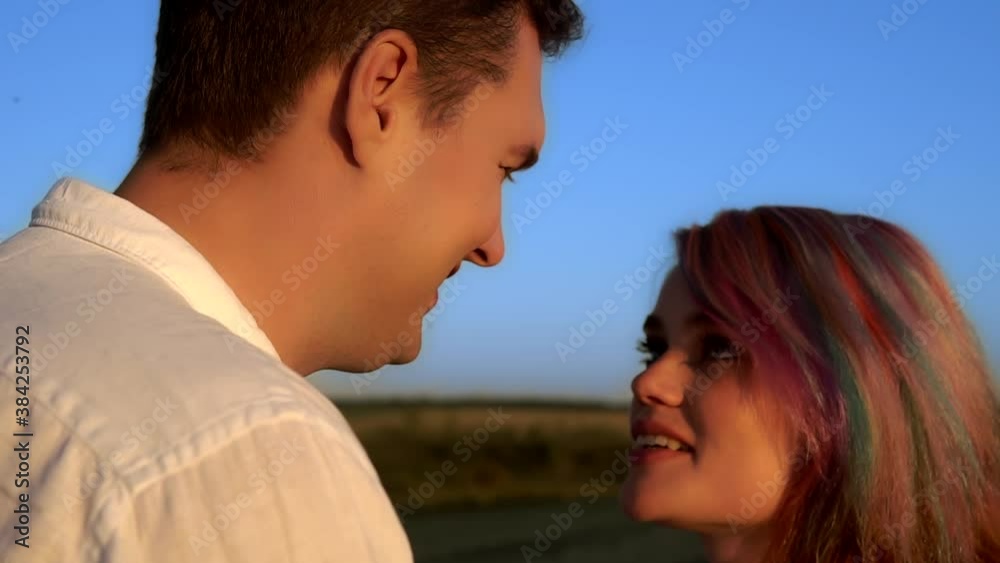 A man and a woman are talking and kissing standing in a summer field in slow motion. Young caucasian couple is smiling and looking at each other with love. Theme of happiness and tender relationship. A man and a woman are talking and kissing standing in a summer field in slow motion. Young caucasian couple is smiling and looking at each other with love. Theme of happiness and tender relationship.