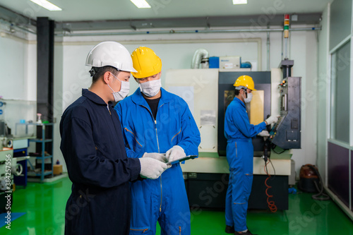 Asian industrial engineers and worker in hard hats discuss product line while using digital tablet and make showing gestures and work in a heavy industry manufacturing factory.