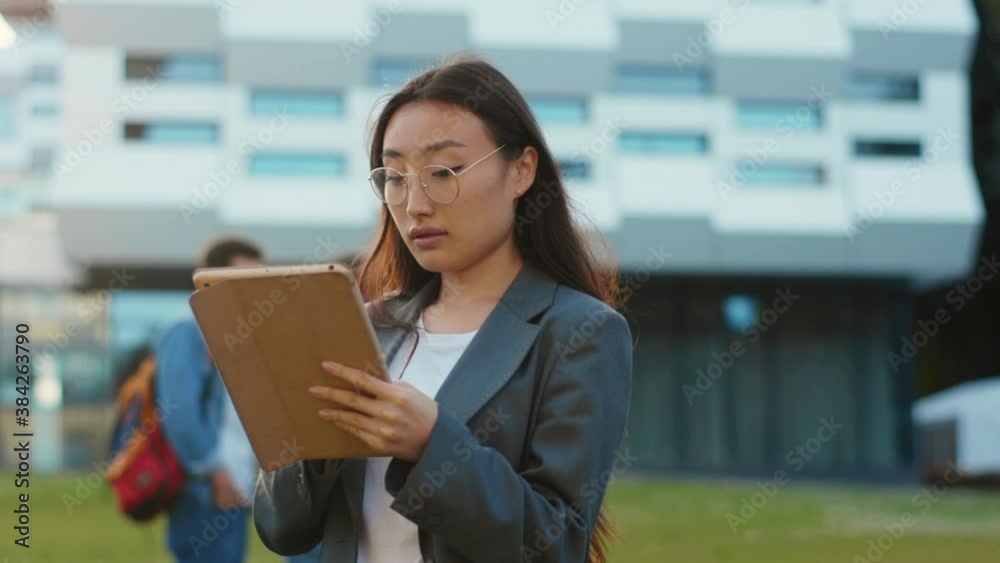 Asian attractive modern girl college student browsing internet tablet computer communicating messaging on break outdoors. Smart generation. University students. Campus. Nature concept.