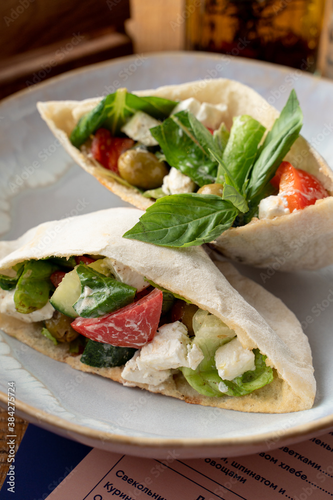 Close up of pita with salad, feta cheese and olives decorated with basil leave on a white plate, close up