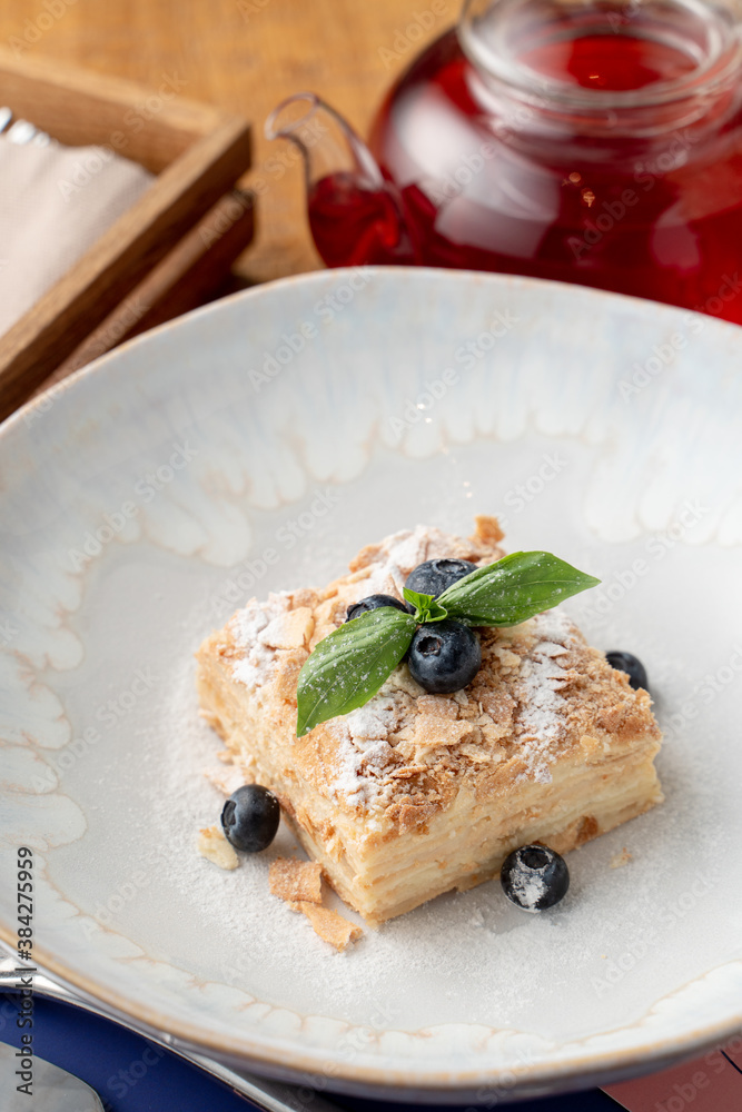 Close up of airy napoleon cake with puff pastry and custard, decorated with blueberry and mint in a fancy restaurant Close up of airy napoleon cake with puff pastry and custard, decorated with blueberry and mint in a fancy restaurant