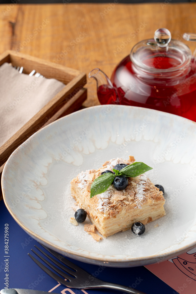 Close up of airy napoleon cake with puff pastry and custard, decorated with blueberry and mint in a fancy restaurant