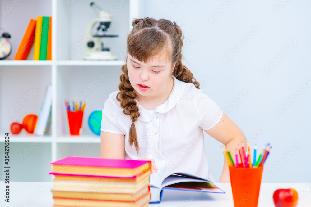 A girl with down syndrome enthusiastically reads a book that lies in front of her on the table. Affordable education for everyone concept A girl with down syndrome enthusiastically reads a book that lies in front of her on the table. Affordable education for everyone concept